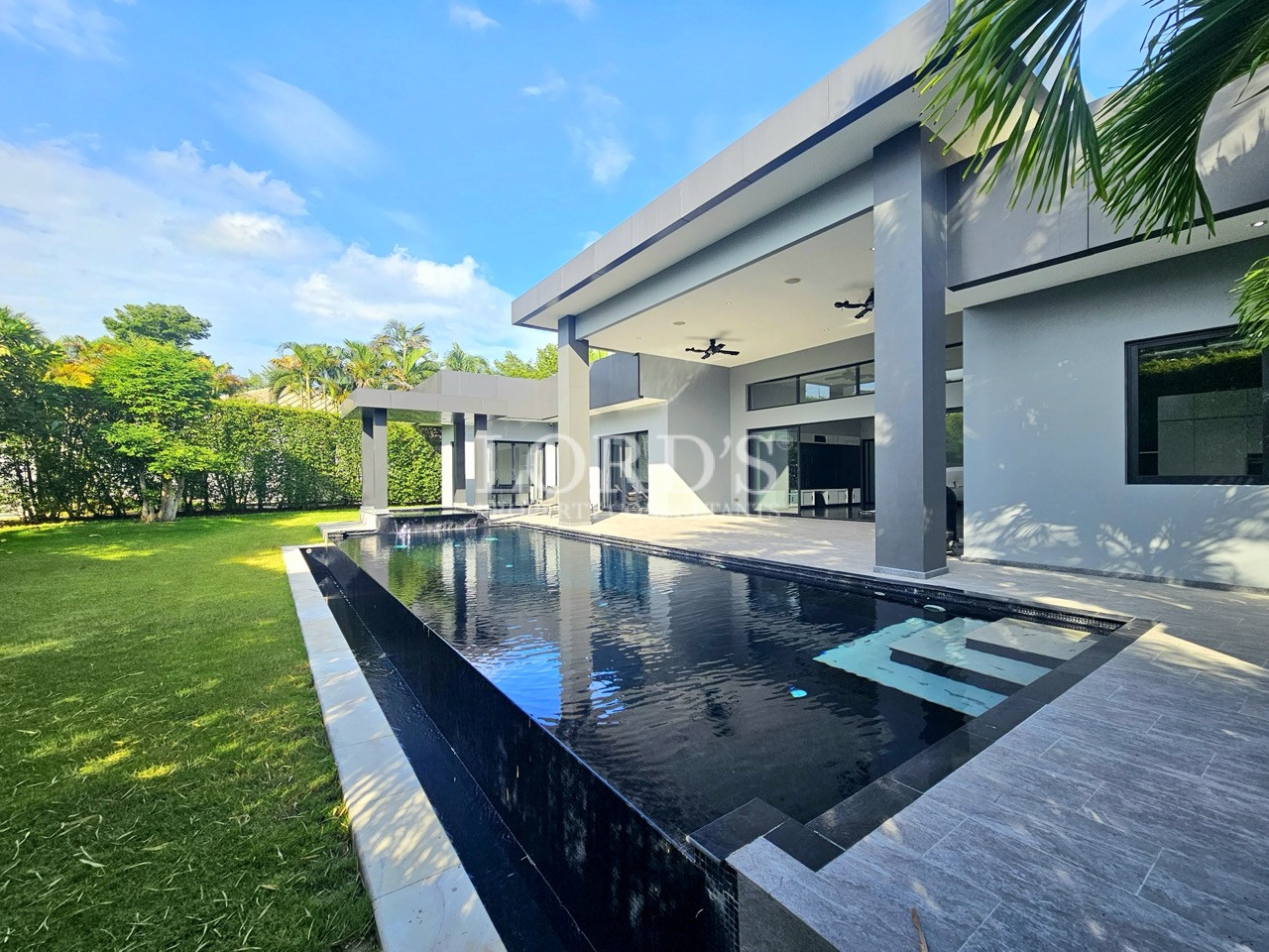 Luxury modern villa with private infinity-style swimming pool, landscaped lawn, covered patio, and contemporary architecture
