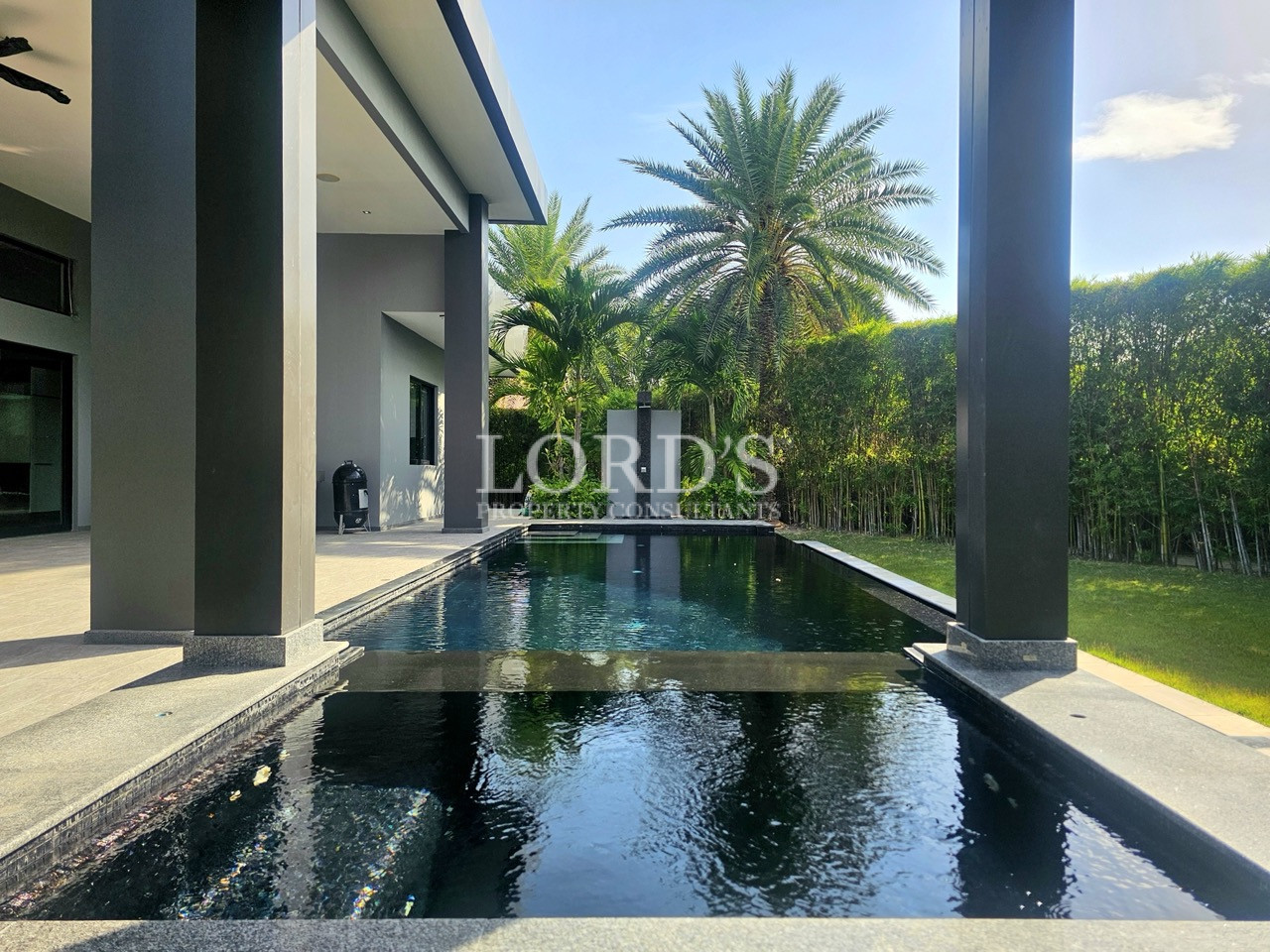 Luxury private swimming pool with modern villa architecture, covered patio, tropical landscaping, and outdoor living space