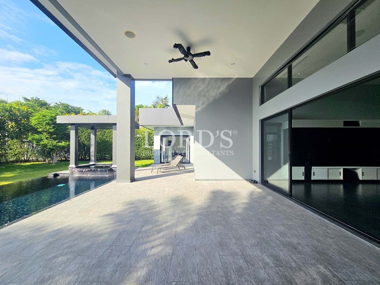 Luxury covered outdoor patio with modern architecture, swimming pool, floor-to-ceiling glass doors, and landscaped garden