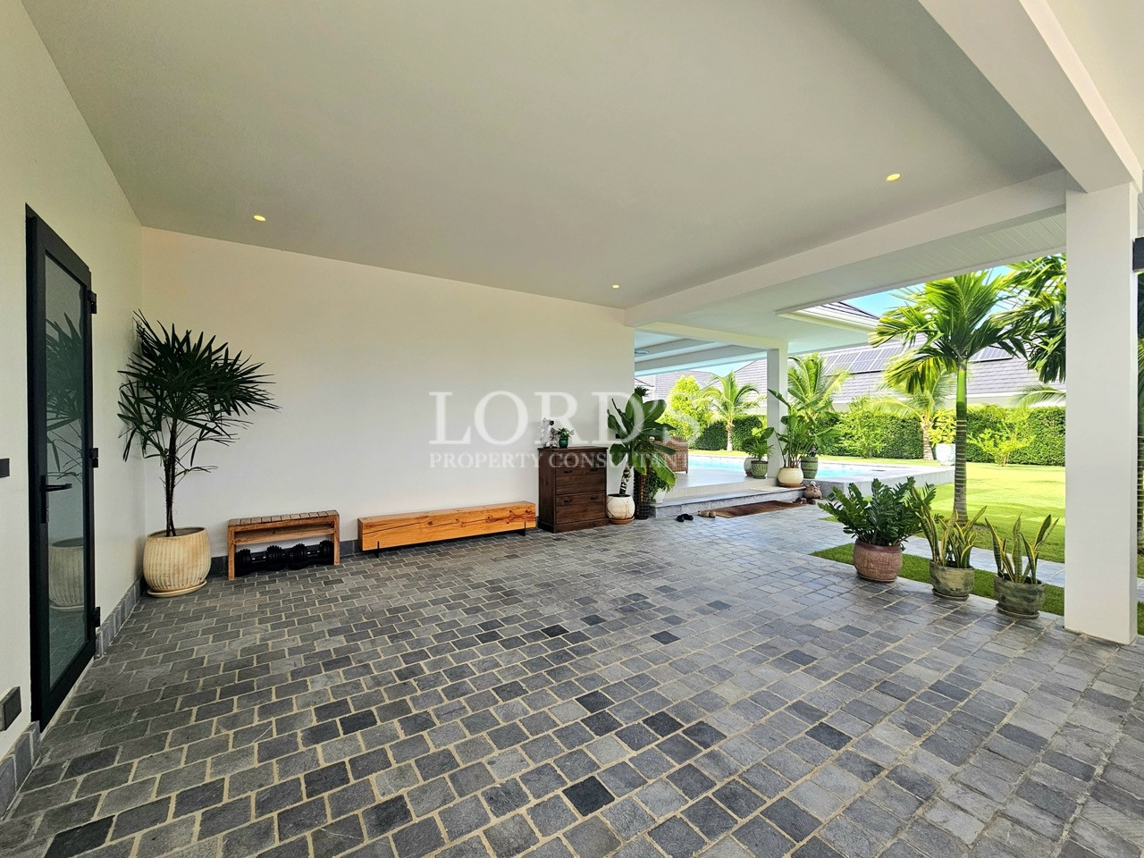 Covered outdoor patio with potted plants, seating, and garden views