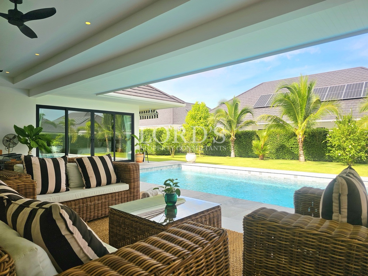 Covered outdoor patio with wicker seating, swimming pool, and tropical garden