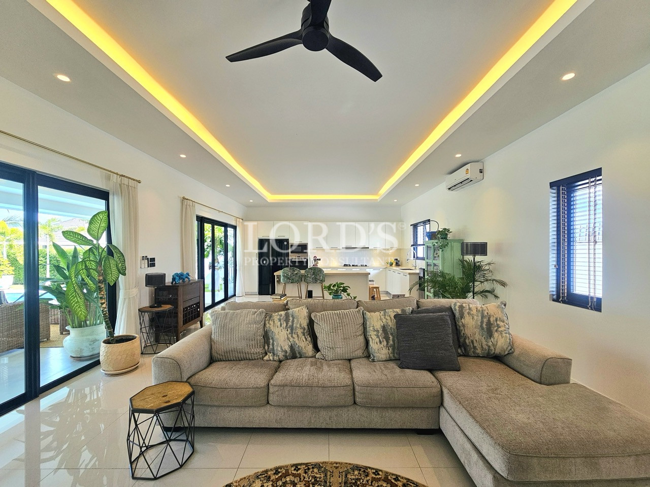 Modern living room with sectional sofa, ceiling fan, and open-plan kitchen