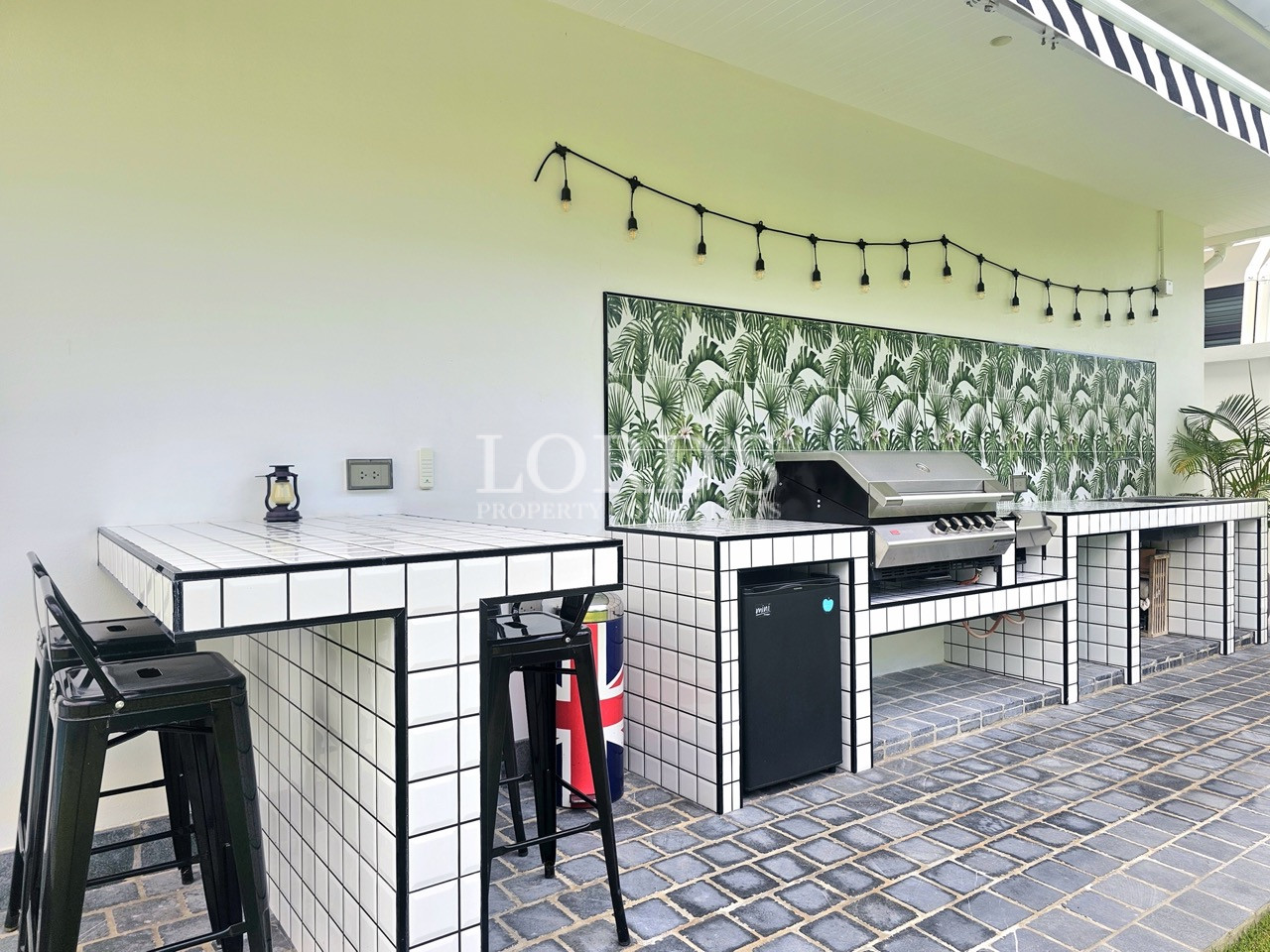 Outdoor kitchen with tiled counters, built-in grill, and bar stools