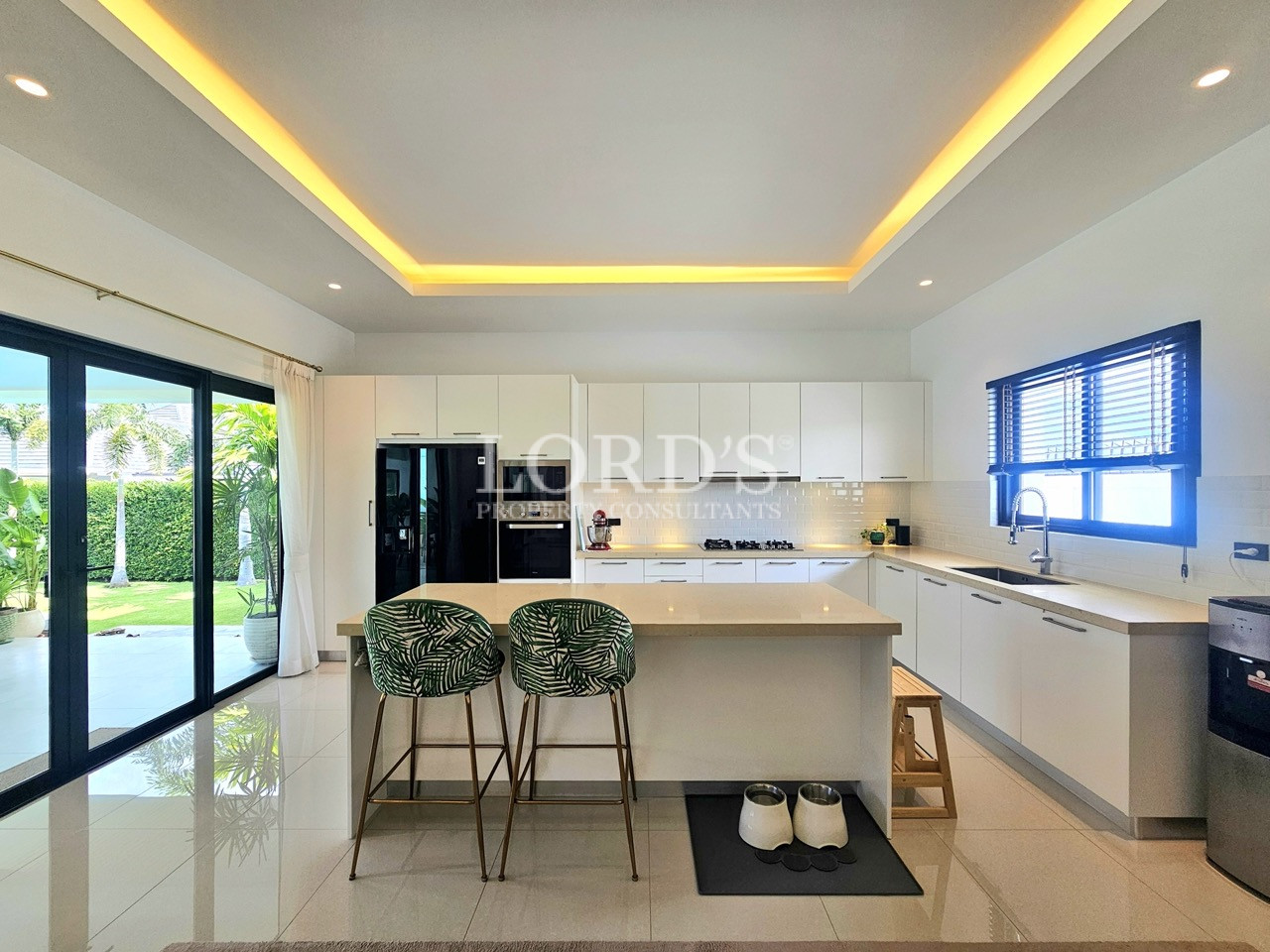 Modern white kitchen with large island, bar stools, and garden views