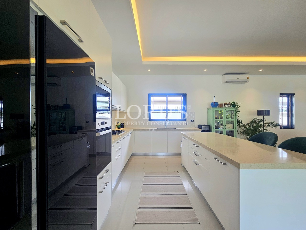 Modern white kitchen with large island, built-in appliances, and dining area