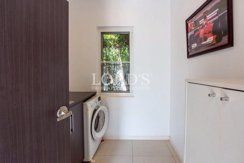 Utility room with a front-loading washing machine, storage cabinets, and a window overlooking greenery