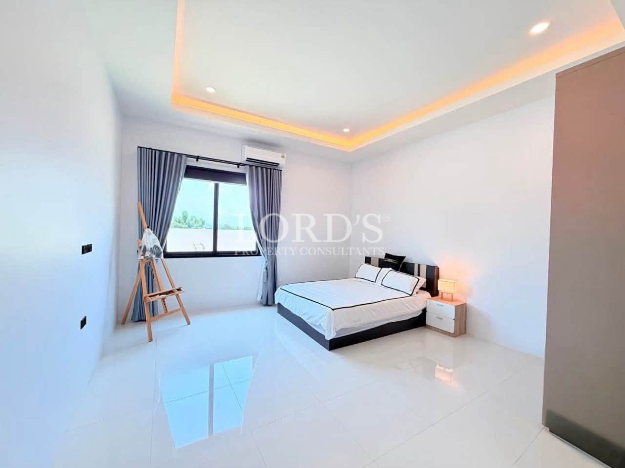 Bright modern bedroom with a minimalist bed, large window, and warm ceiling lighting