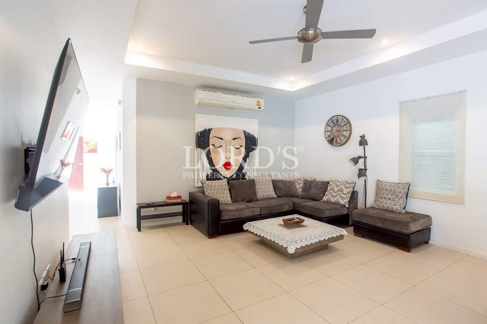 Bright modern living room with an L-shaped sectional sofa, wall-mounted TV, ceiling fan, air conditioning, and coffee table
