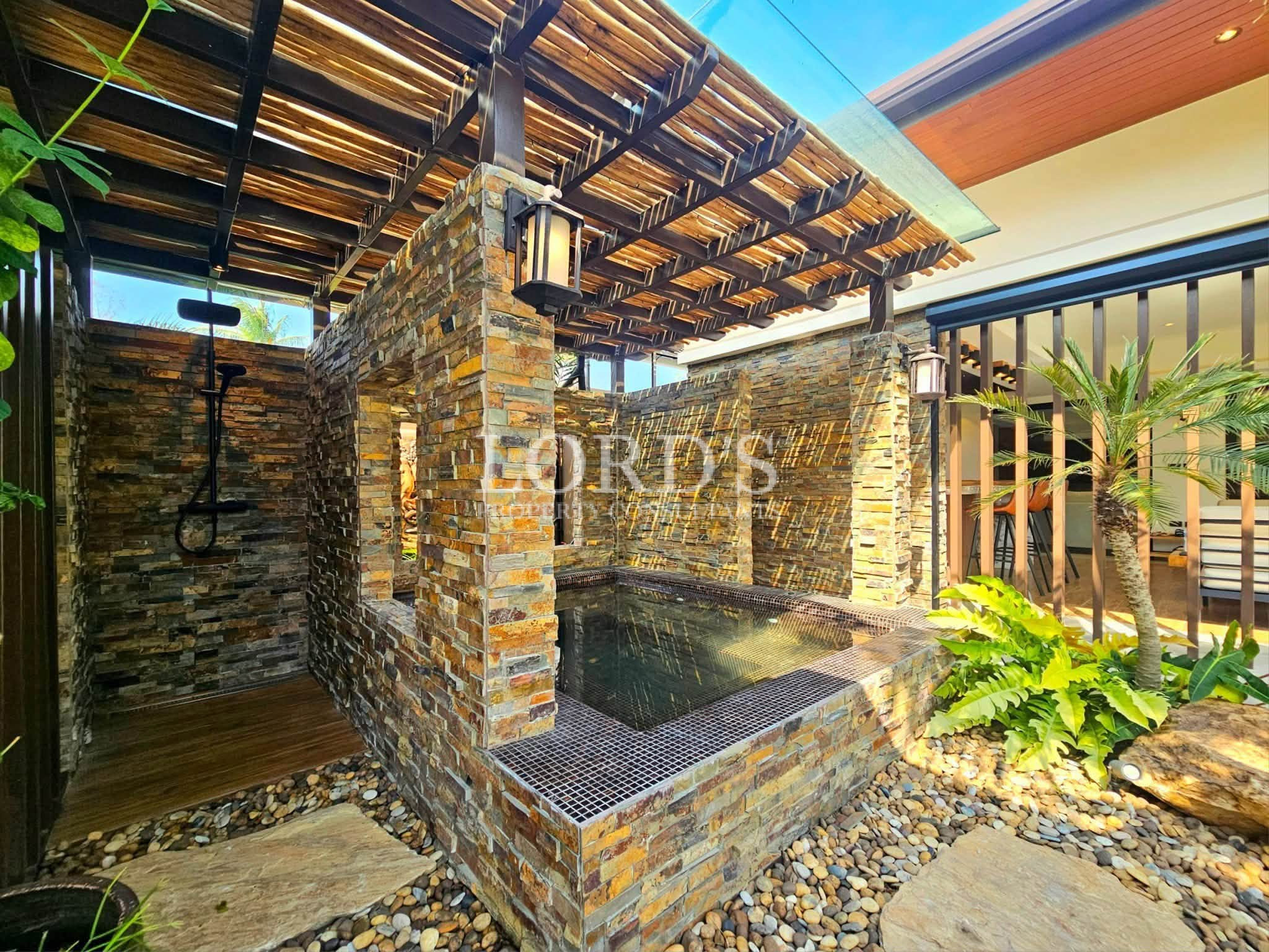 Luxury outdoor spa courtyard with natural stone walls, soaking pool, rain shower, tropical landscaping, and timber pergola