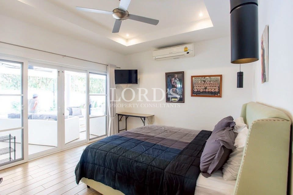 Bright modern bedroom with a king-size bed, ceiling fan, air conditioning, TV, and large glass doors