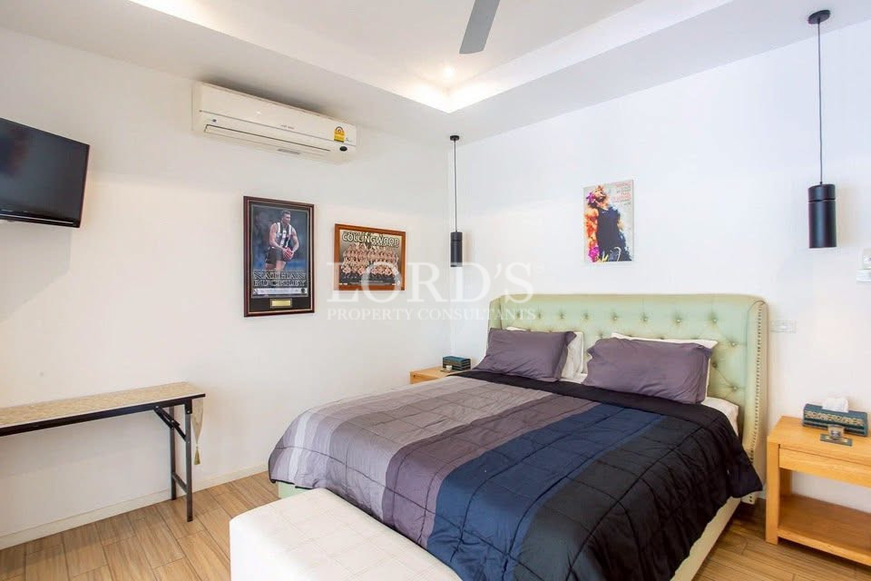 Bright bedroom with upholstered bed, bedside tables, wall-mounted TV, and air conditioning