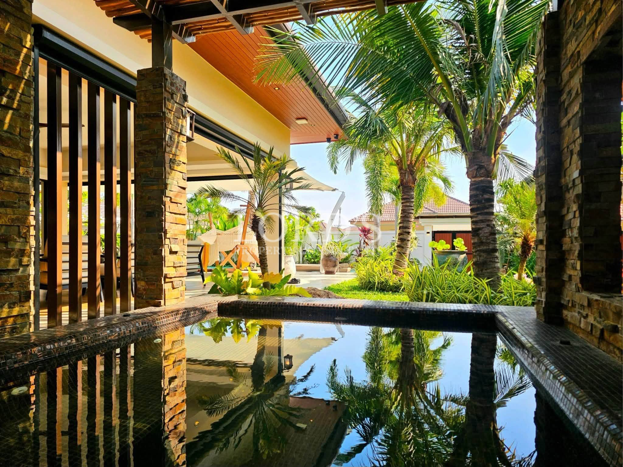 Luxury tropical villa courtyard with reflective water feature, natural stone columns, lush palm trees, and landscaped garden