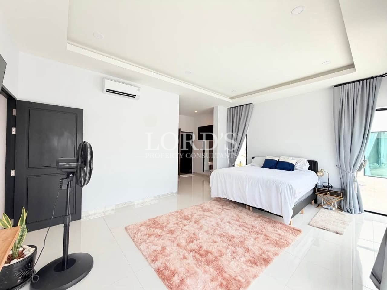 Modern spacious bedroom with a king-size bed, soft gray curtains, and a pink area rug