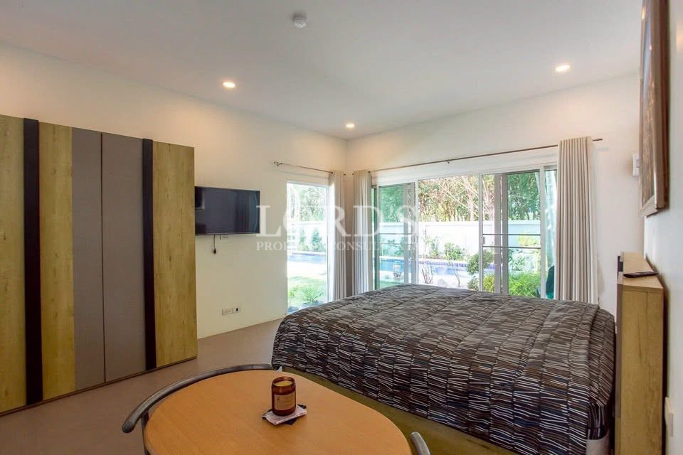 Bright bedroom with king-size bed, built-in wardrobe, TV, and pool view