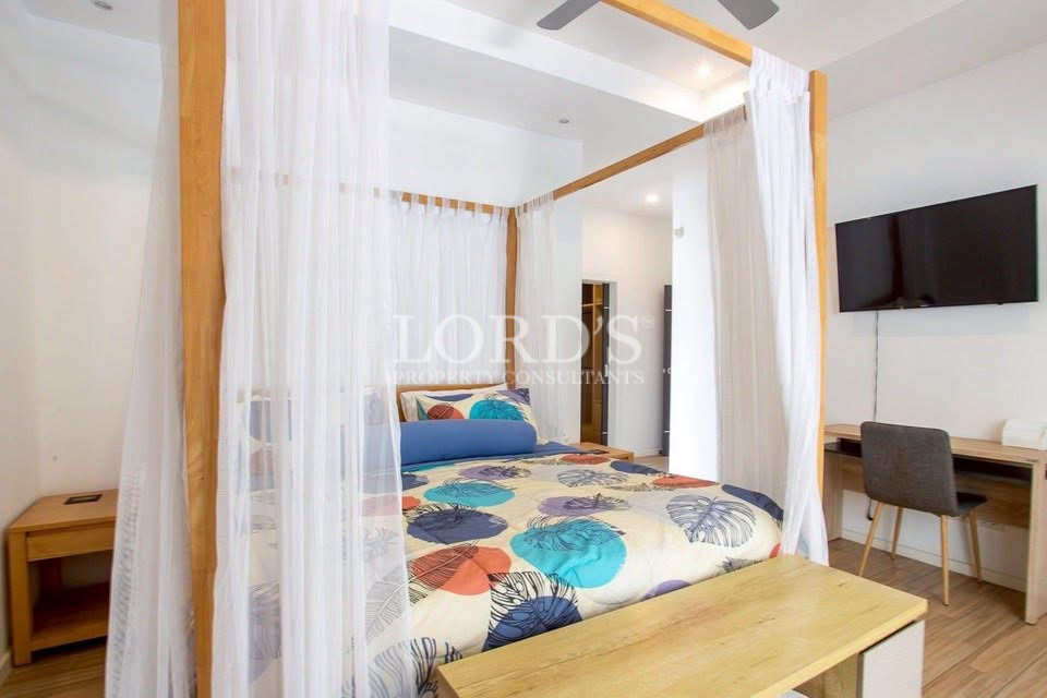 Bright bedroom with four-poster bed, sheer curtains, desk, and wall-mounted TV