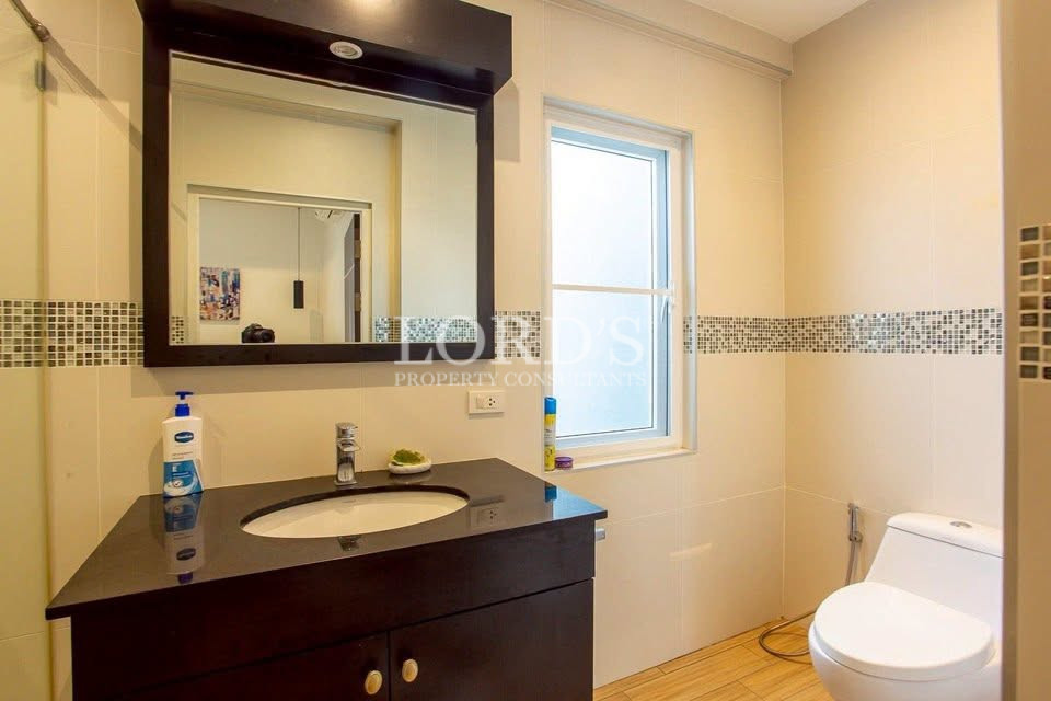 Modern bathroom with dark vanity, oval sink, mirror, frosted window, and toilet