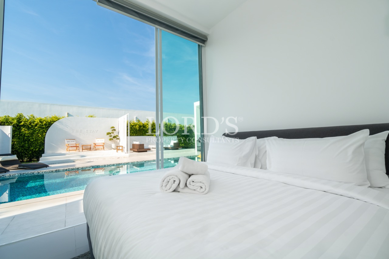 Modern bedroom with white bed overlooking a private swimming pool