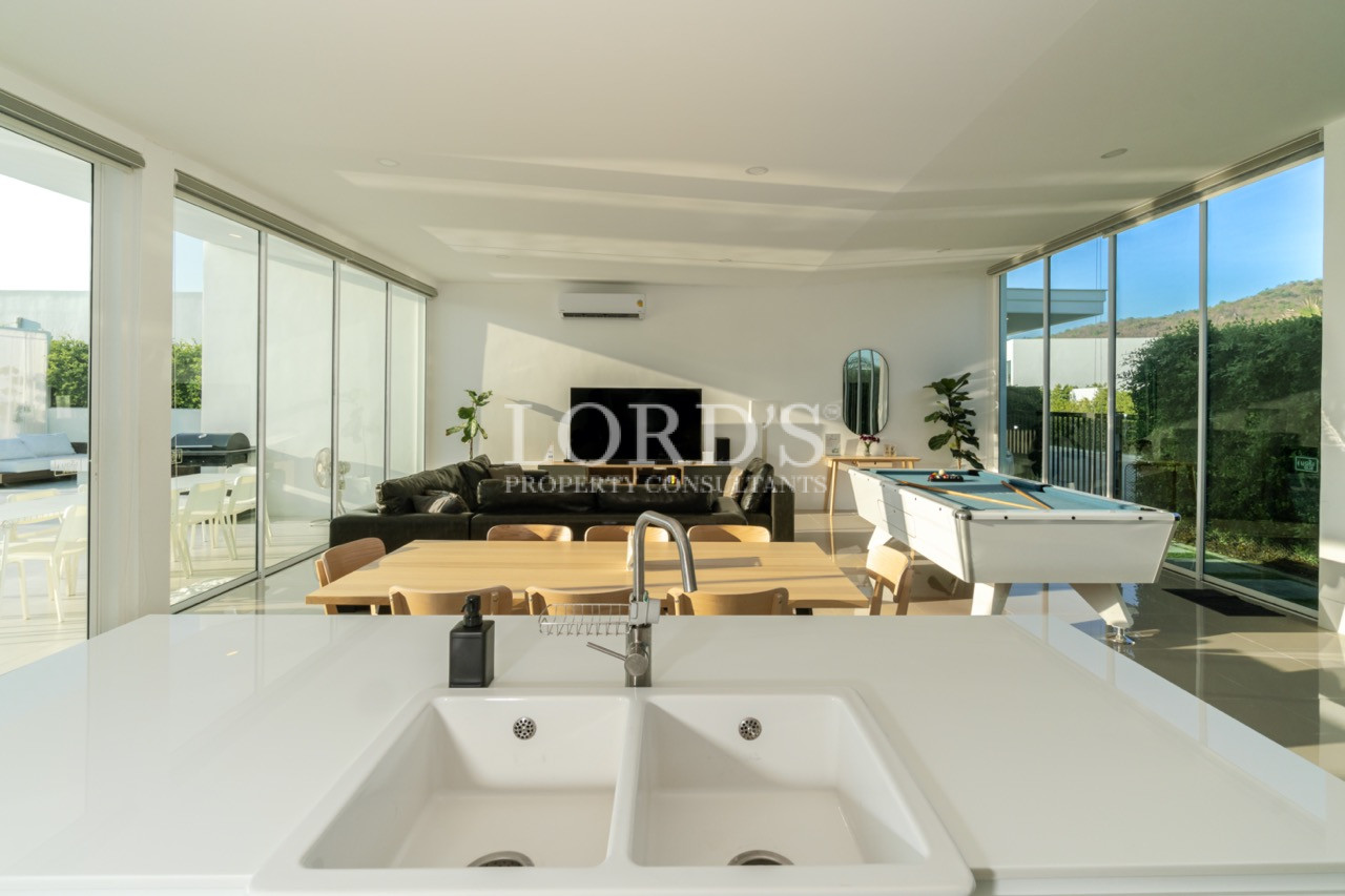 Modern open-plan kitchen and living area with island sink, dining table, sofa, and pool table