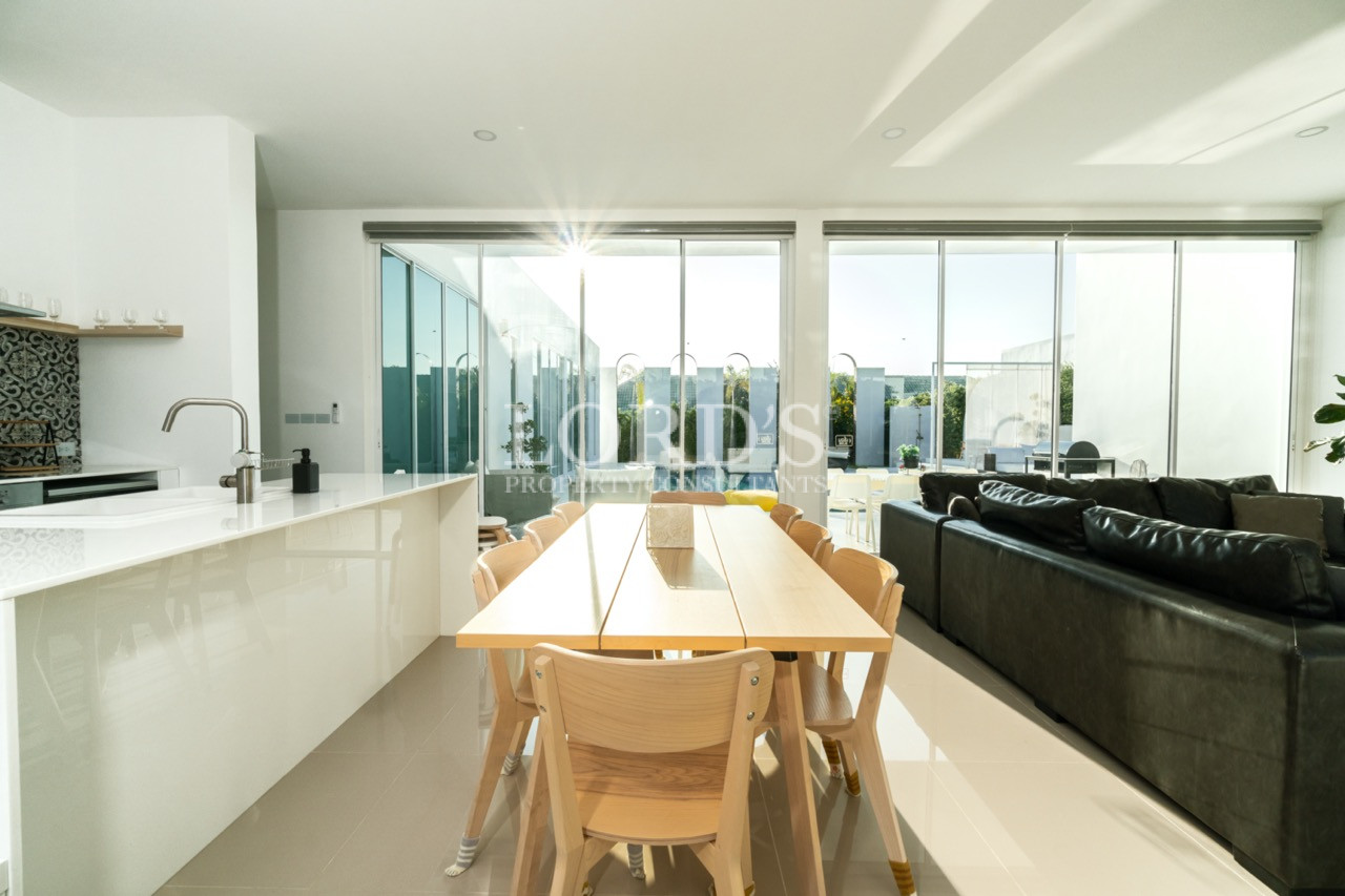 Modern open-plan kitchen and dining area with wooden table, black sofa, and large glass windows