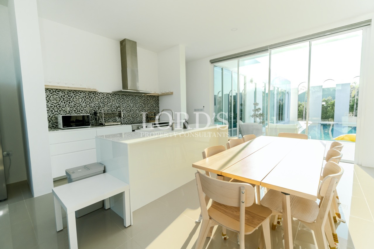 Modern kitchen and dining area with white island, wooden table, and large glass doors