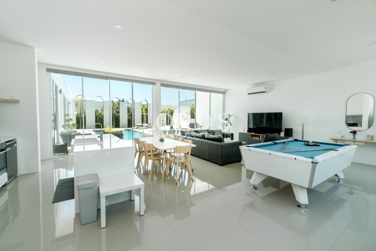 Modern open-plan living room with pool table, dining area, kitchen, and large glass windows