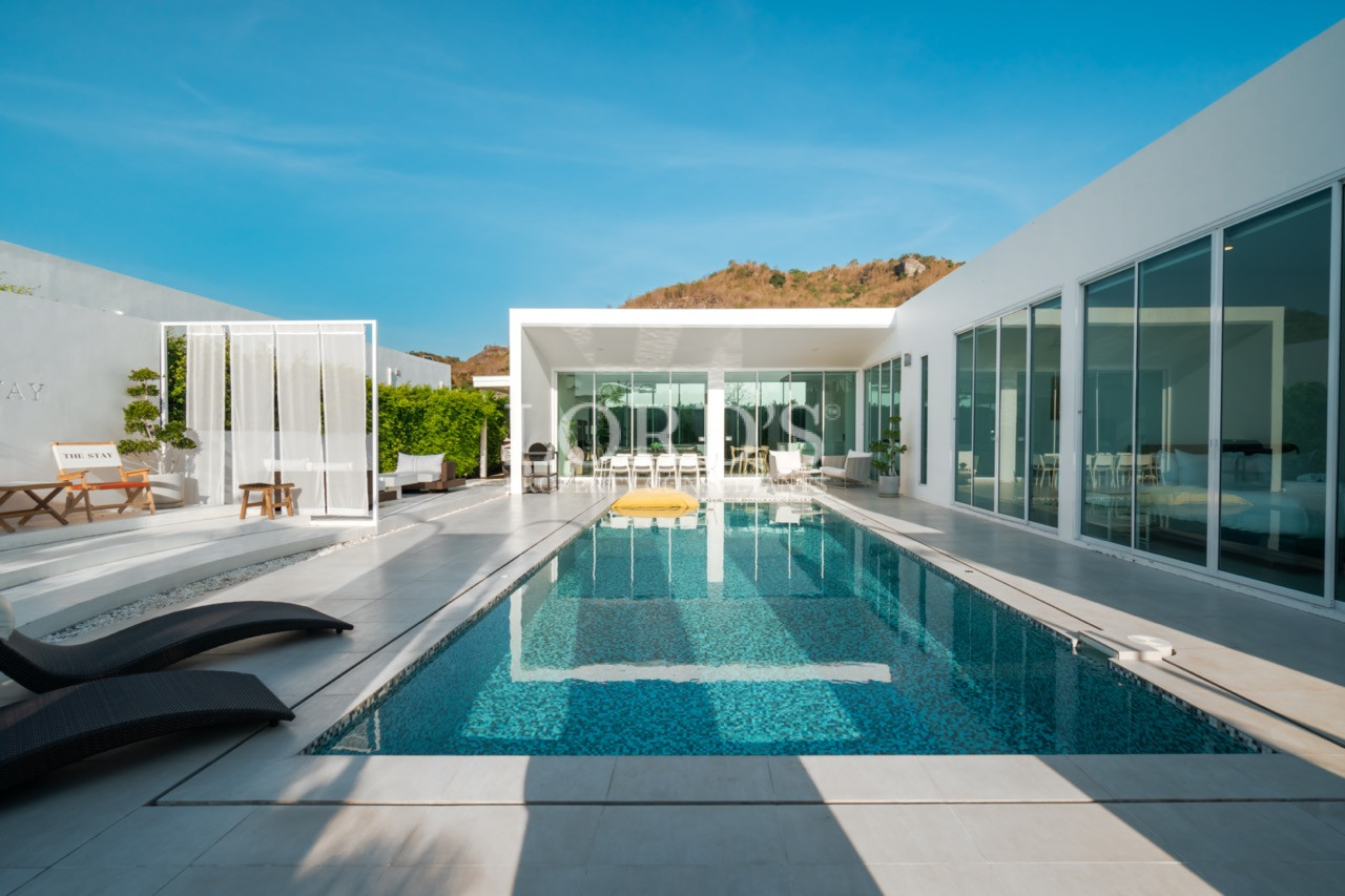 Modern private villa with long swimming pool, sun loungers, and glass-walled rooms