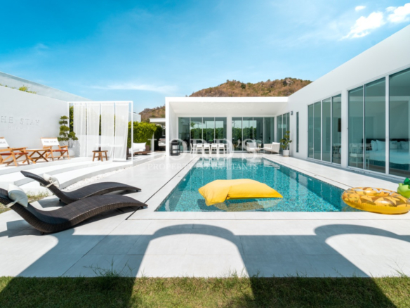 Modern private villa with swimming pool, sun loungers, and glass-walled living area
