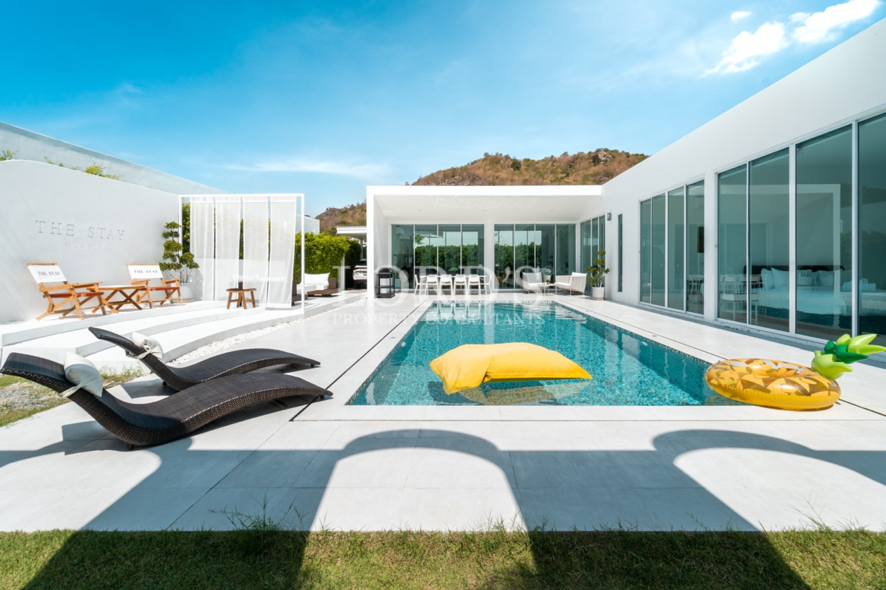 Modern private villa with swimming pool, sun loungers, and glass-walled living area