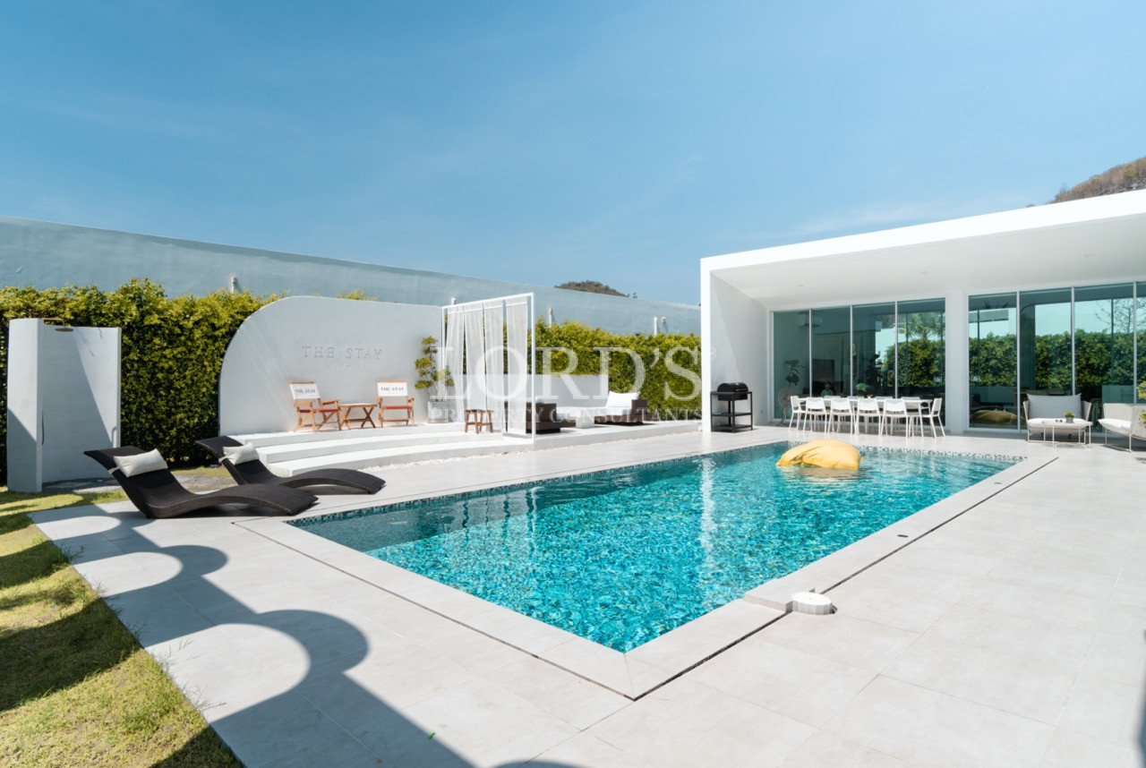Modern private villa pool with sun loungers and open-plan glass living area