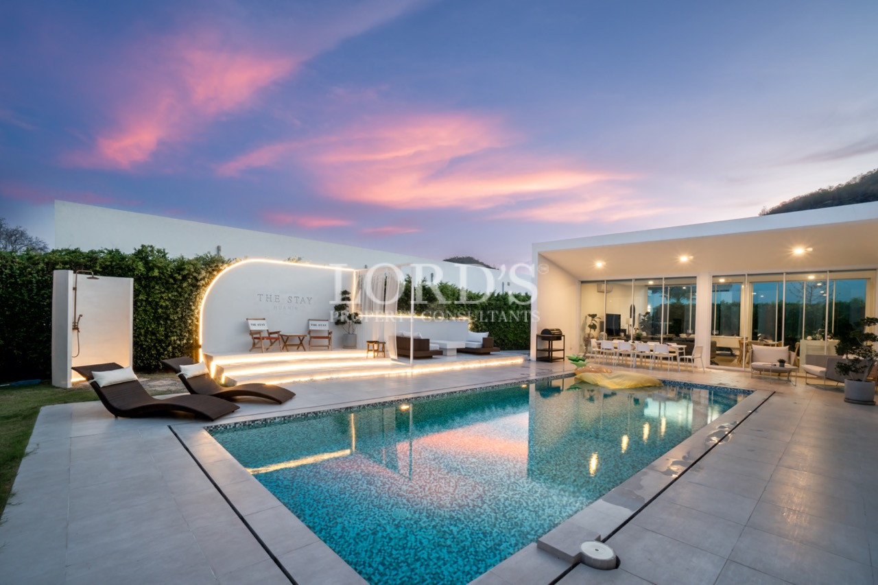 Luxury villa pool at sunset with outdoor lounge area and glass-walled living space
