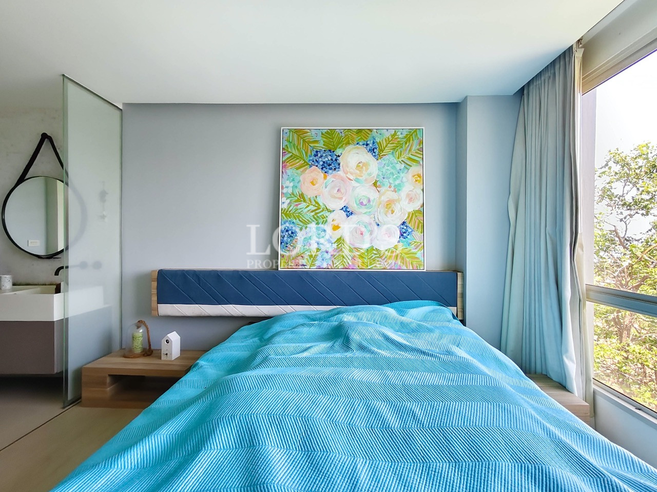 Modern bedroom with large windows, contemporary furnishings, and an open vanity area with glass partition