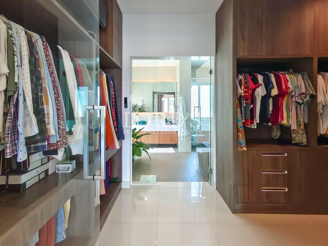 Luxury walk-in closet with custom wooden wardrobes, organized clothing storage, and direct access to a spa-inspired bathroom