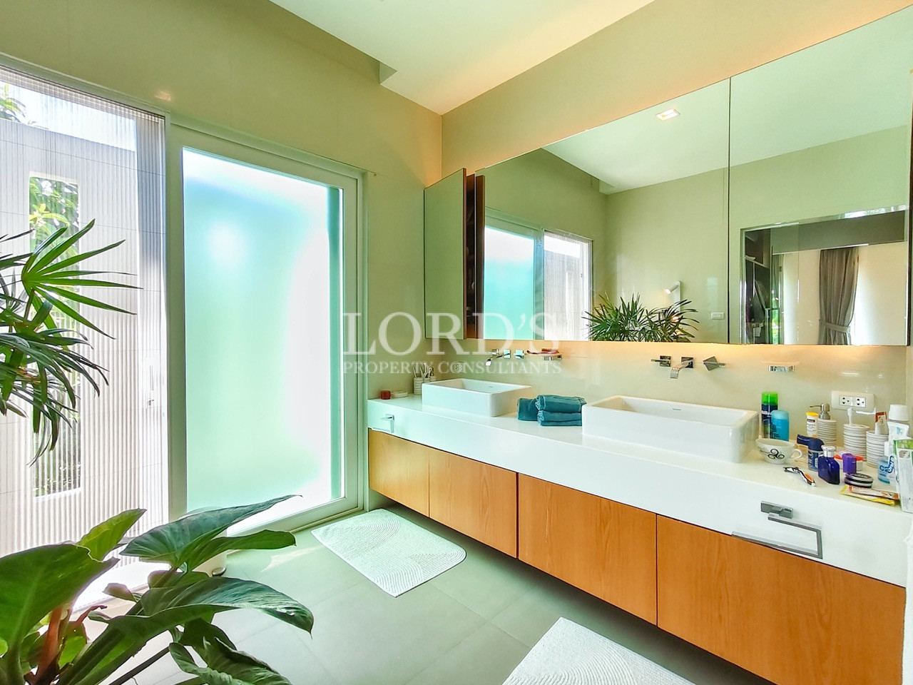 Luxury double vanity bathroom with floating cabinets, large mirror, frosted glass door, and modern design