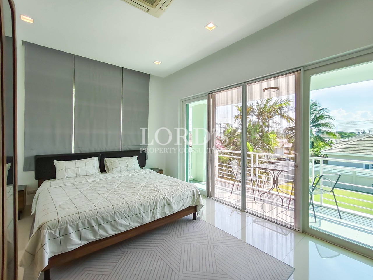 Luxury master bedroom with king-size bed, private balcony, floor-to-ceiling sliding glass doors, and garden view
