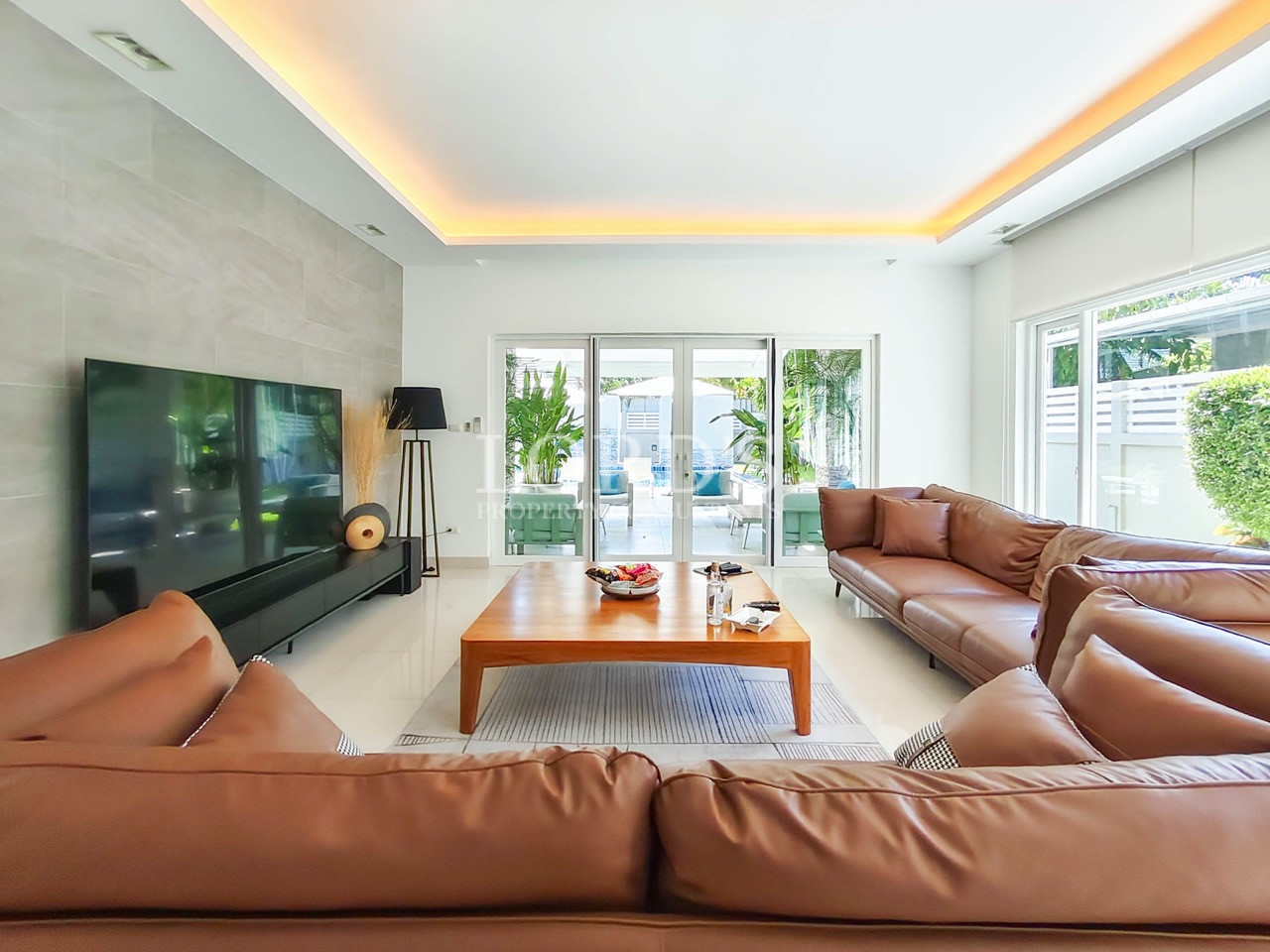 Luxury modern living room with leather sofas, large TV, wooden coffee table, and garden view
