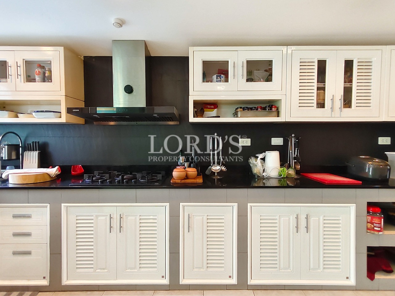 Luxury modern kitchen with white cabinets, black granite countertop, gas cooktop, and built-in range hood