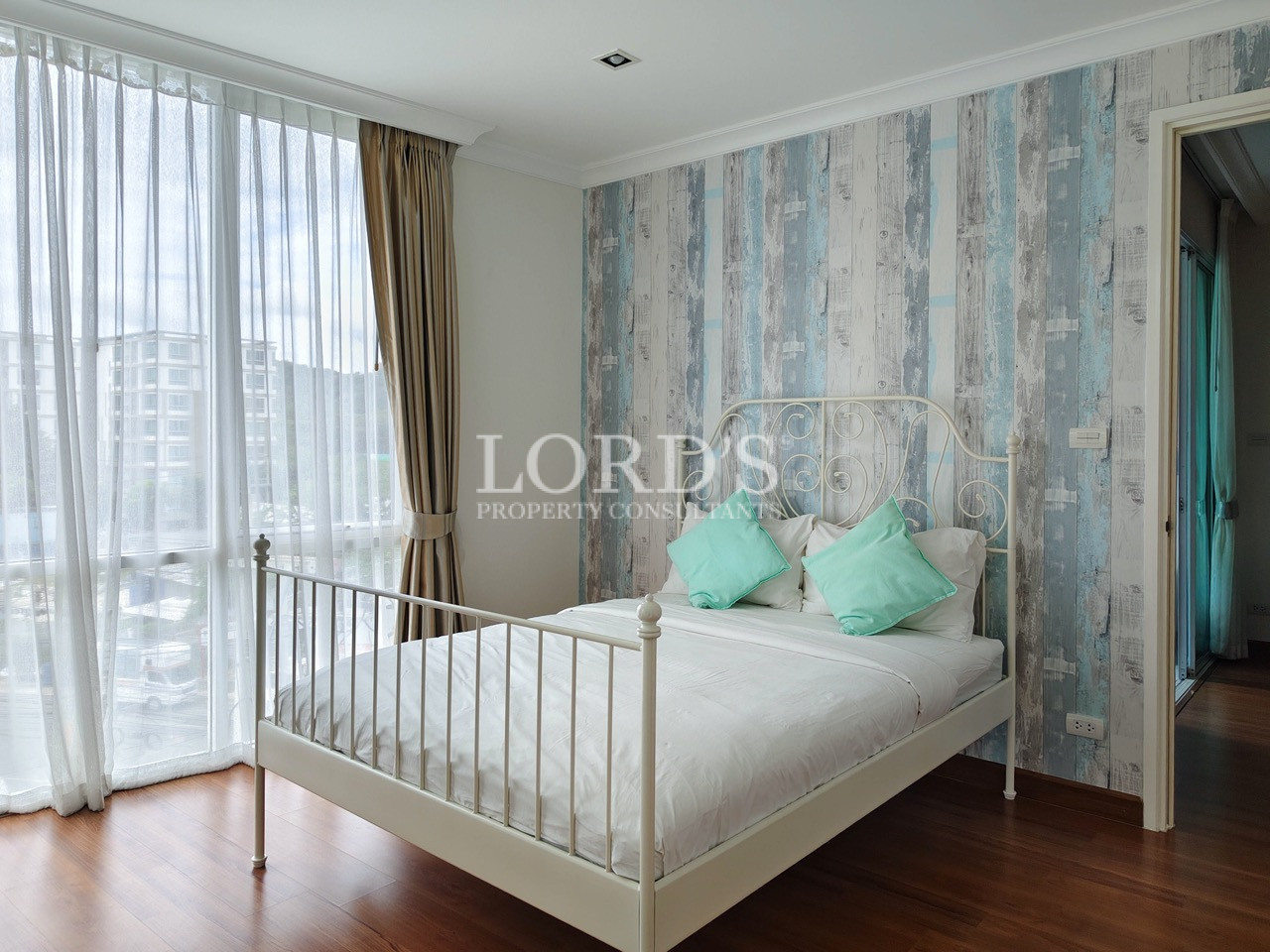 Bright bedroom with a white metal bed, mint green pillows, large windows, and a blue-gray accent wall