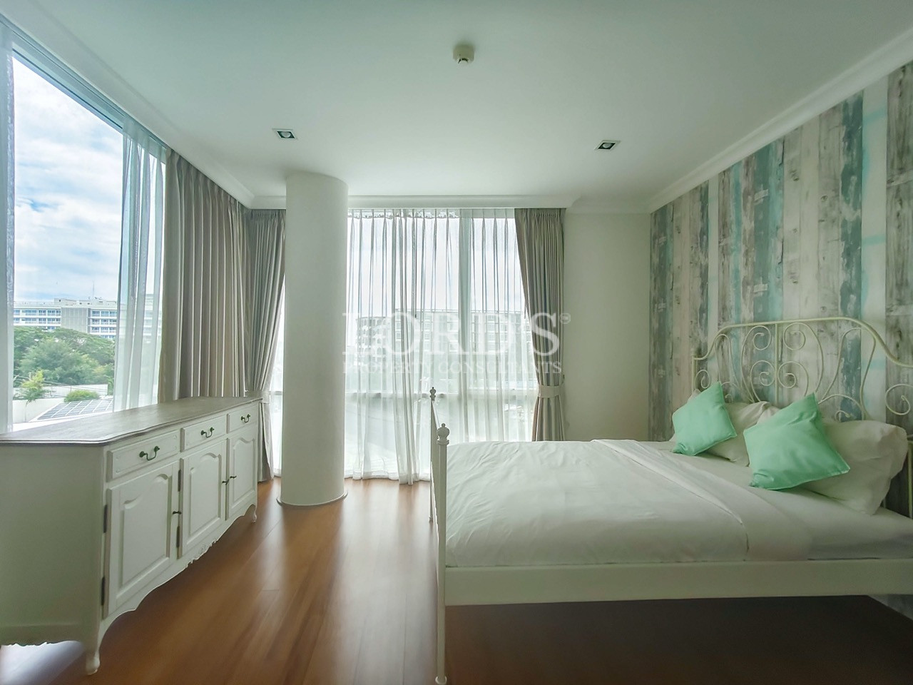 Bright bedroom with a white metal bed, mint green pillows, large windows, and a decorative accent wall