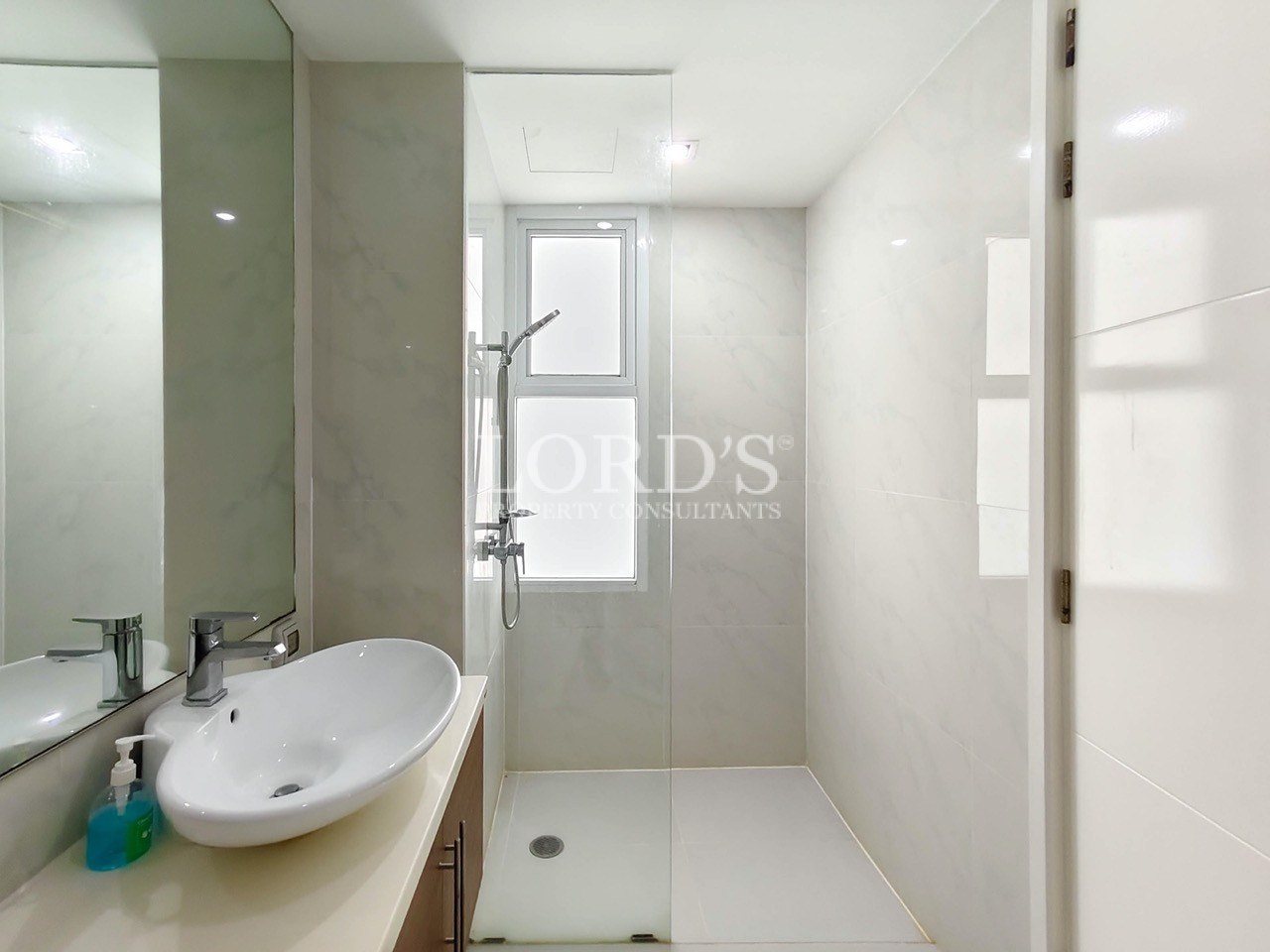 Modern bathroom with a glass shower enclosure, white vanity, mirror, and marble-style tiles