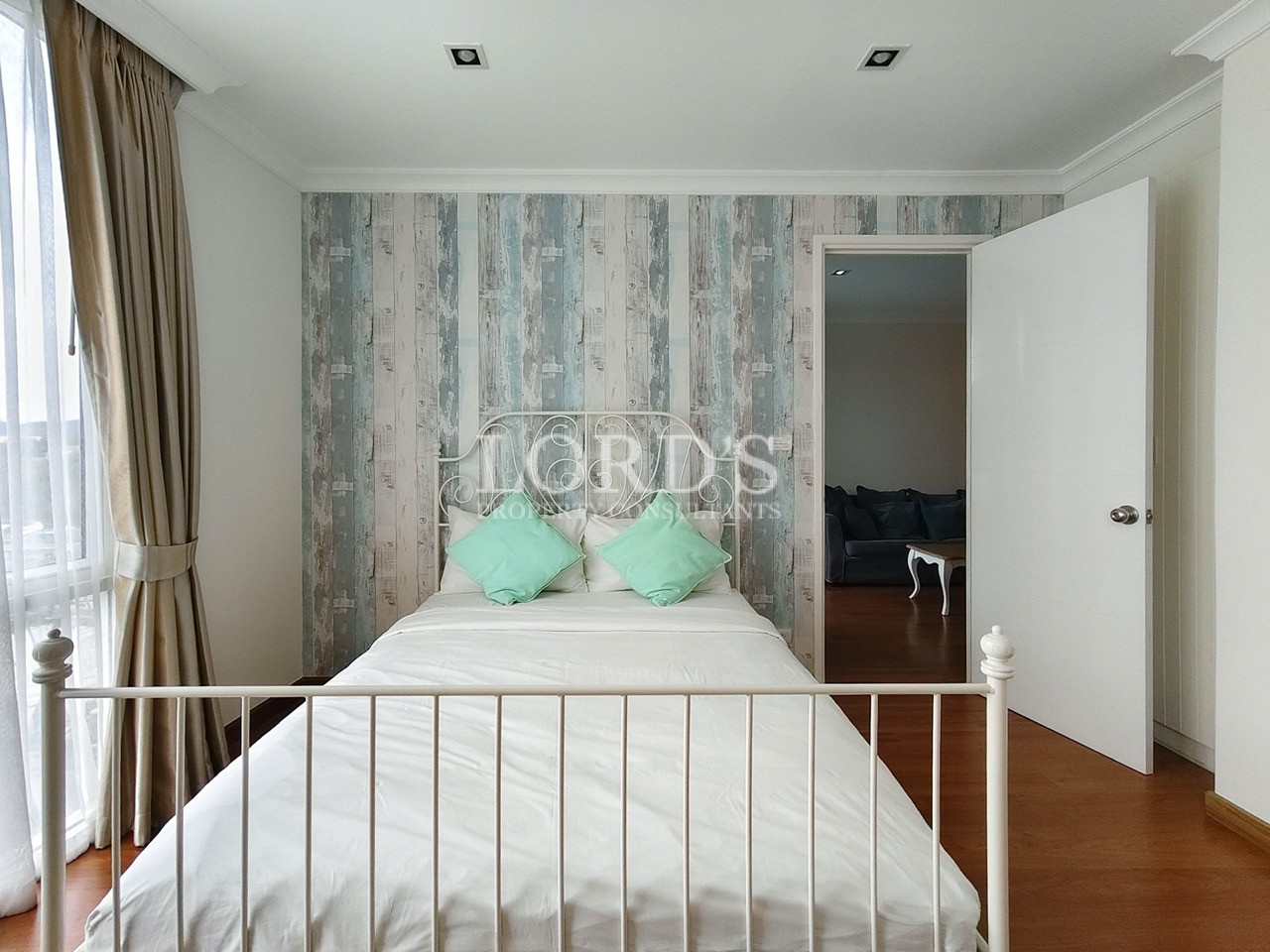 Bright bedroom with a white metal bed, patterned accent wall, and beige curtains