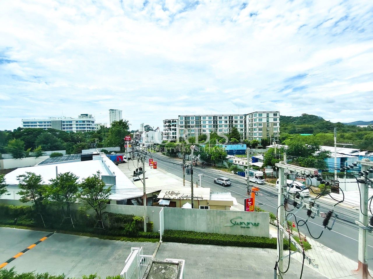 Panoramic city view with a busy road, residential buildings, greenery, and distant hills