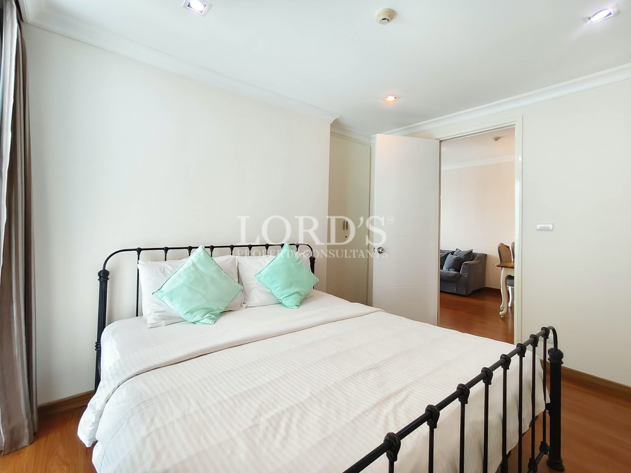 Bright modern bedroom with black metal bed, white bedding, wooden flooring, and adjoining living area