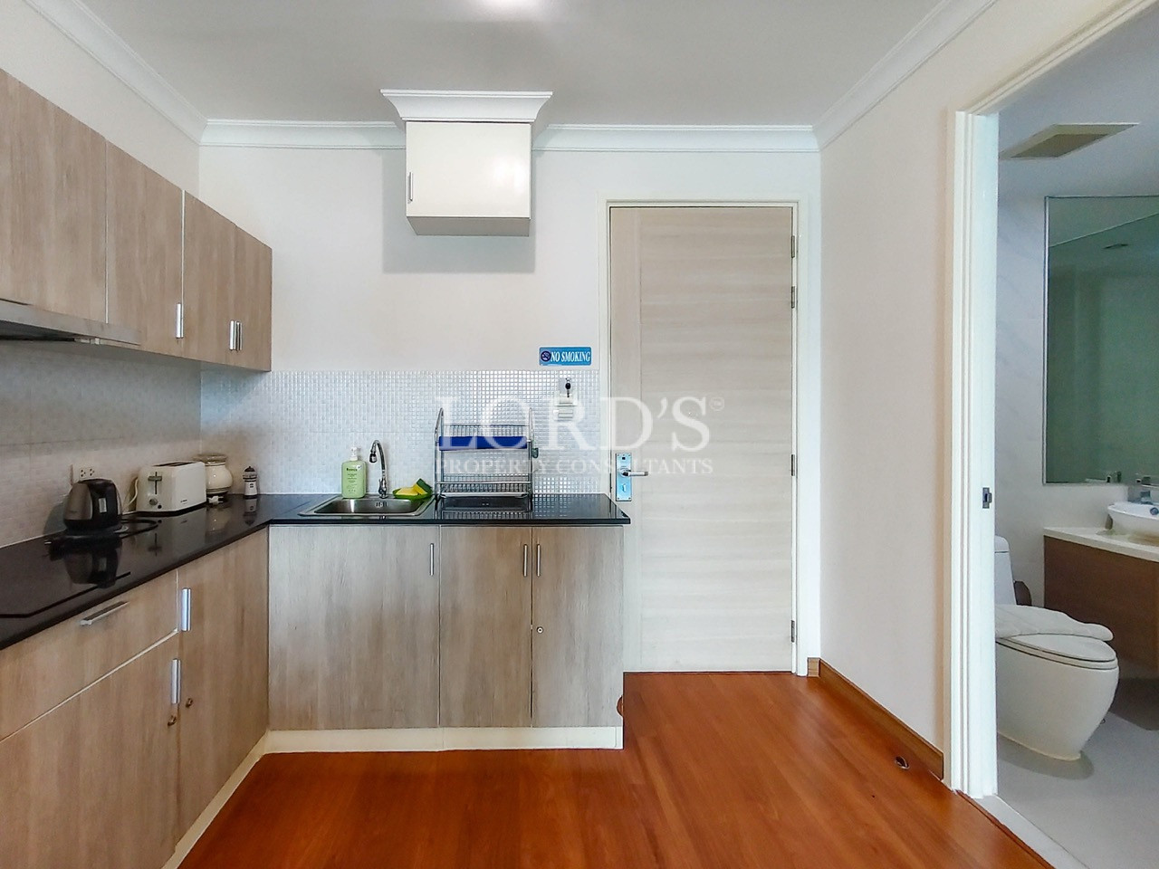 Modern apartment kitchen with light wood cabinets, black countertop, sink, and stainless steel appliances