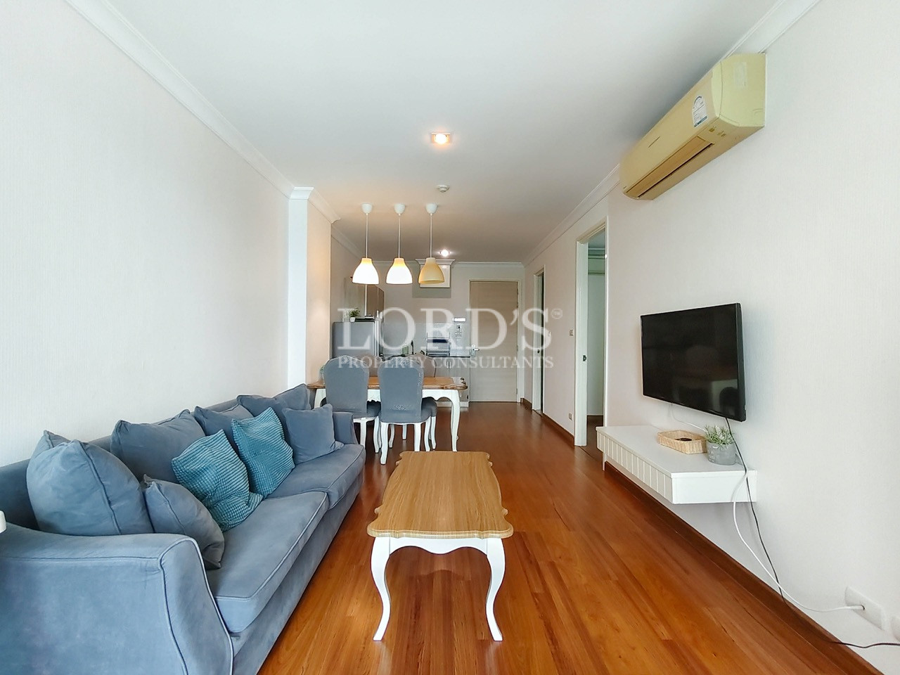 Modern living room with blue sofa, wooden flooring, TV, dining area, and air conditioning