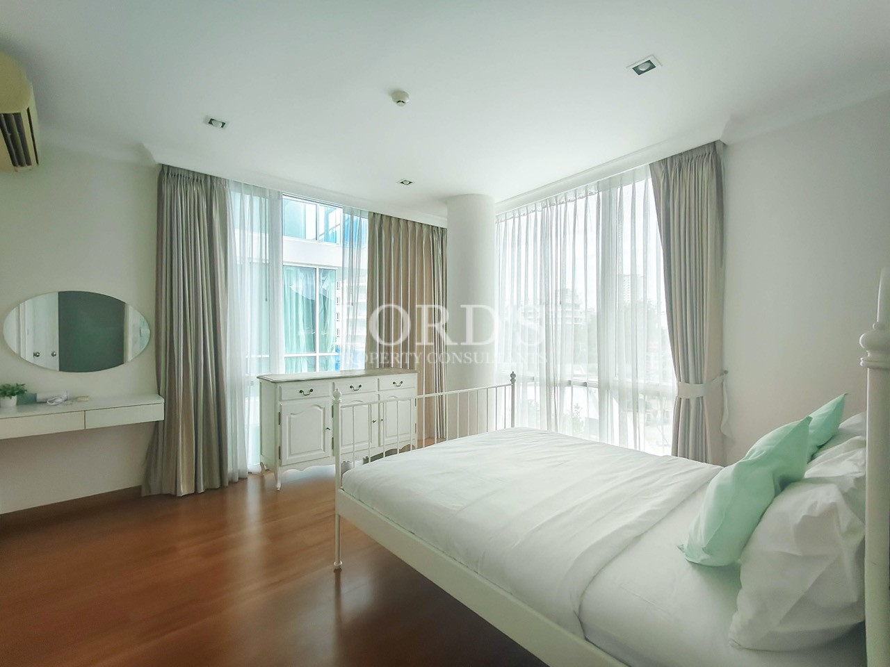 Bright modern bedroom with floor-to-ceiling windows, white bed, elegant curtains, and wooden flooring
