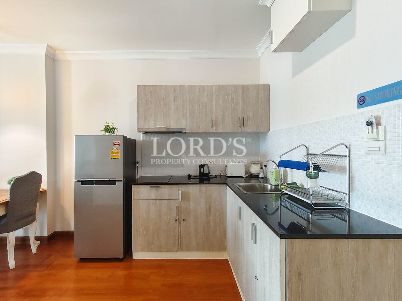 Modern compact kitchen with wood cabinetry, black countertops, stainless steel refrigerator, and double sink