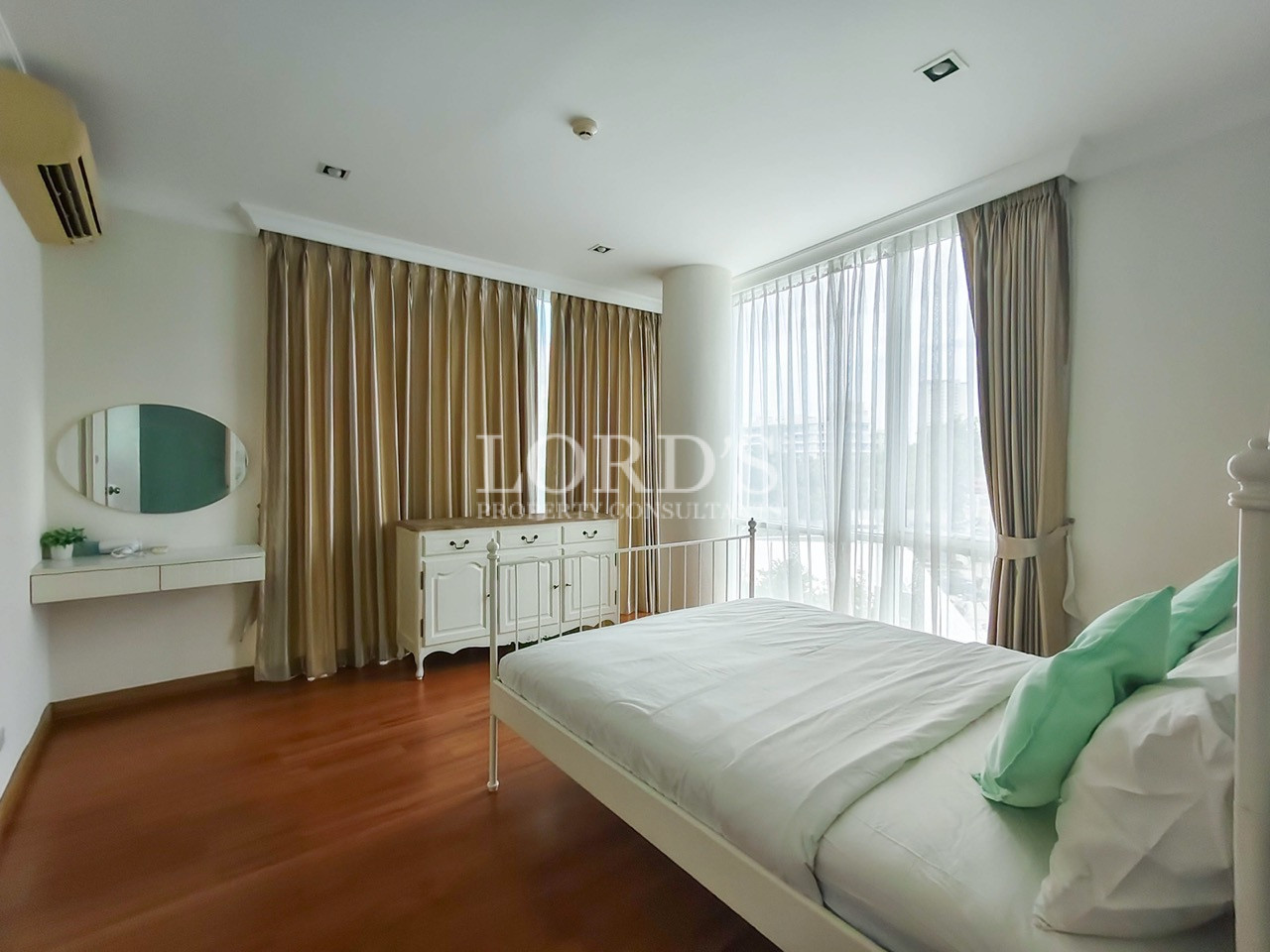 Bright modern bedroom with a white bed, floor-to-ceiling windows, curtains, and wooden flooring
