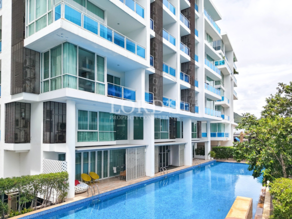Modern resort apartment building with blue glass balconies and a large outdoor swimming pool