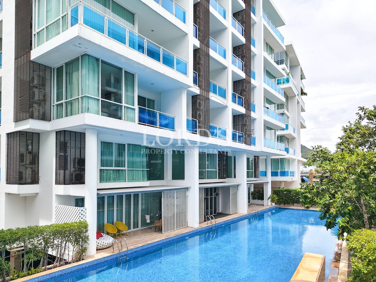 Modern resort apartment building with blue glass balconies and a large outdoor swimming pool