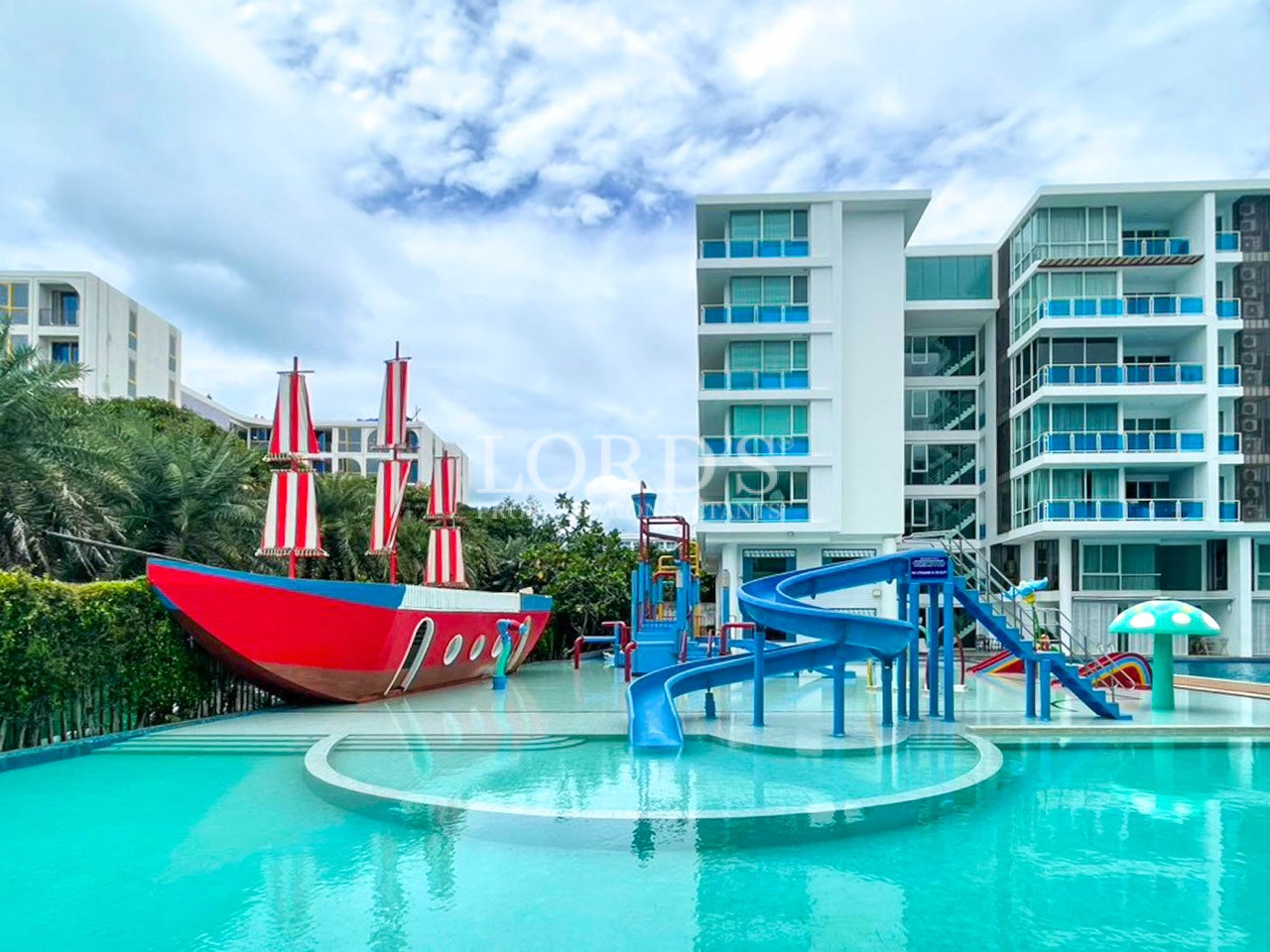 Resort swimming pool with water slides, a pirate ship play area, and modern hotel buildings
